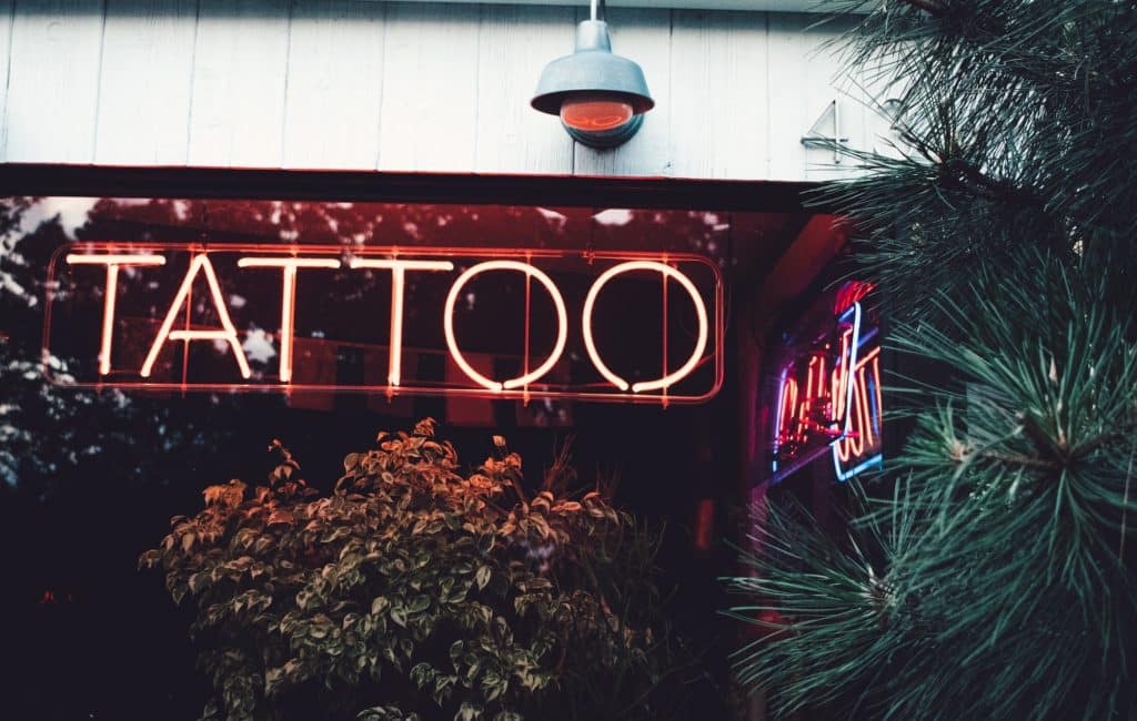 A neon sign that reads tattoo posted up on a shop