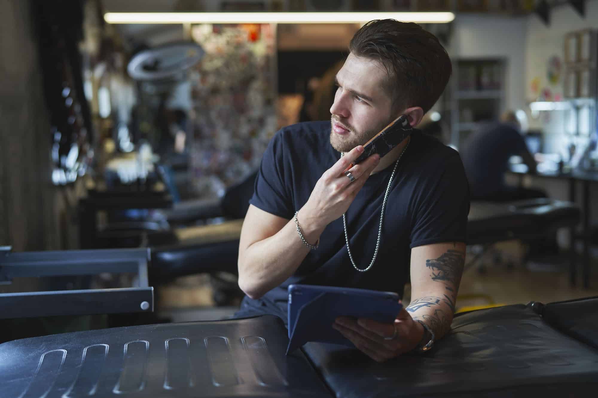 Caucasian tattoo artist talking by mobile phone and in tattoo studio