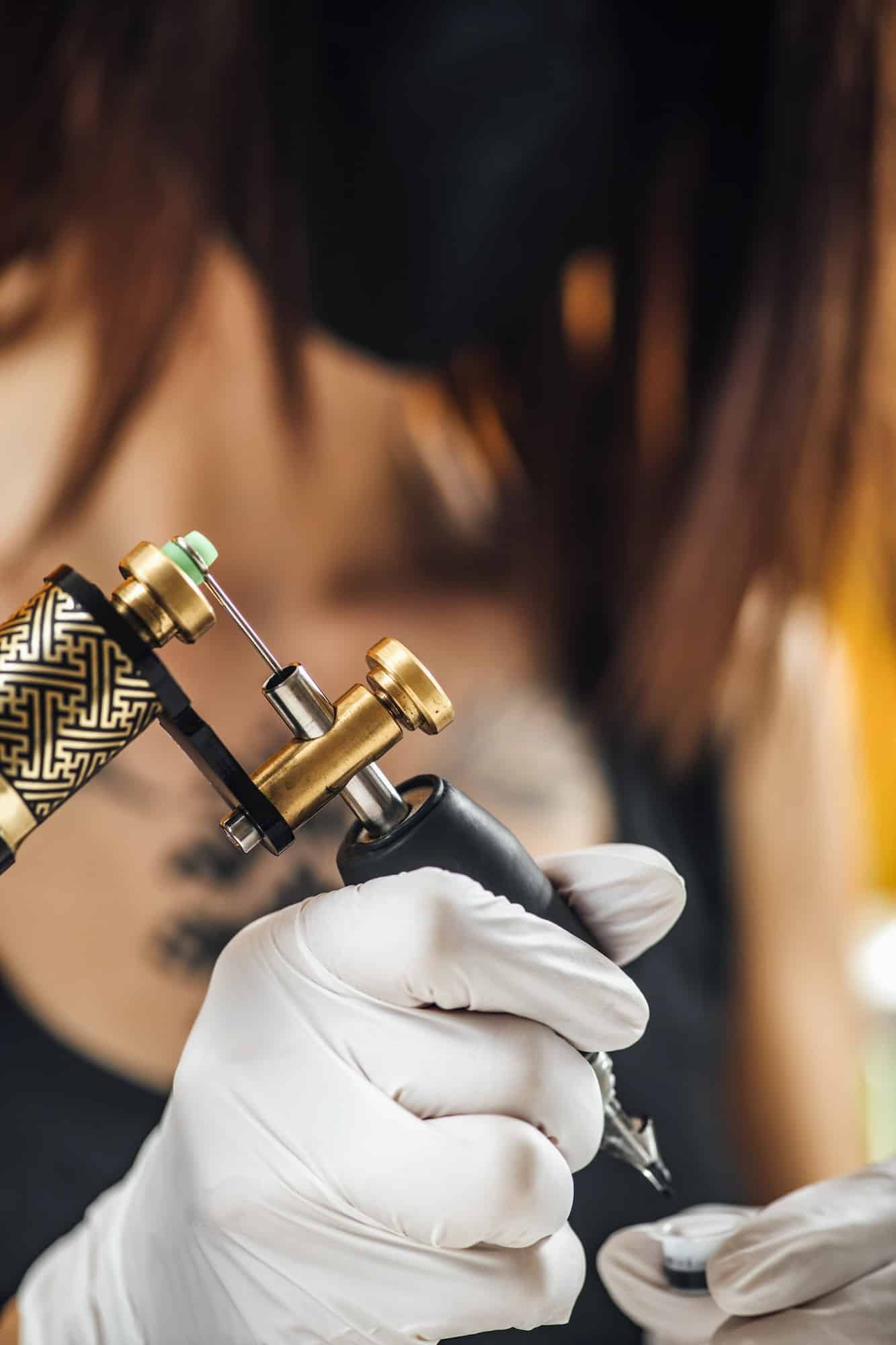 Female Tattoo Artist Prepares Tattoo Machine for Making a Tattoo on a Men’s Arm