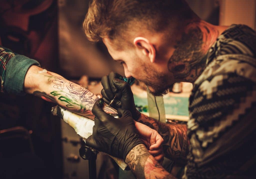 Tattoo artist makes a tattoo on a man's hand.
