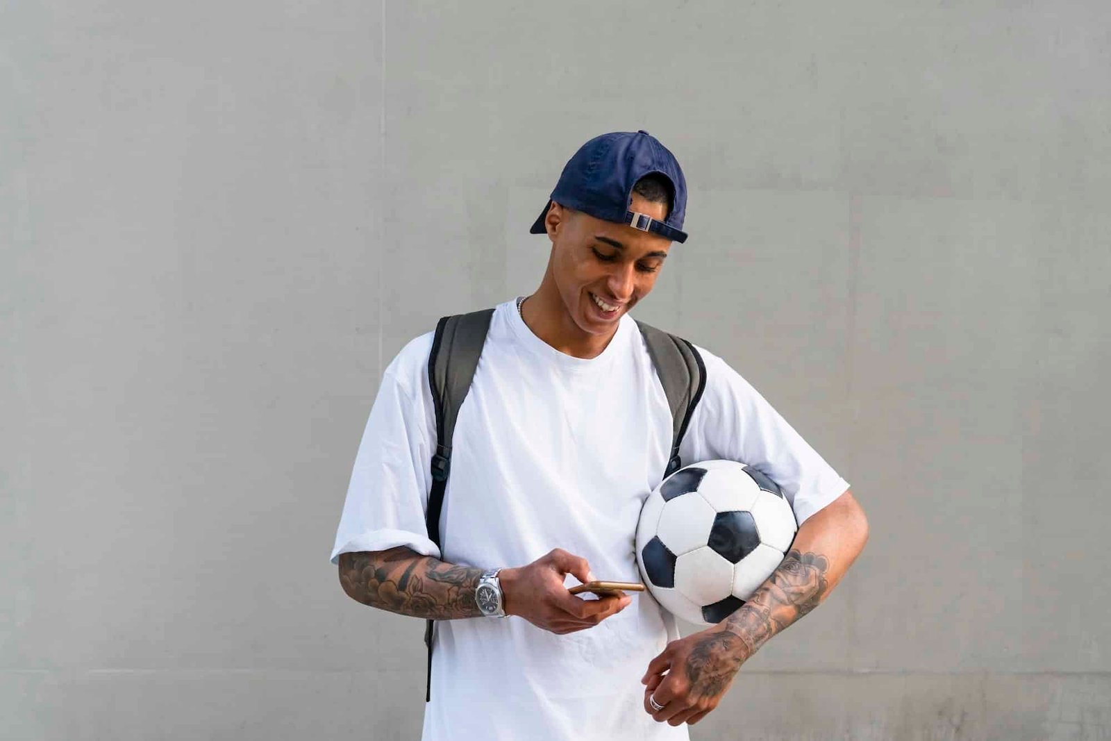 Tattooed young man with football alooking at smartphone