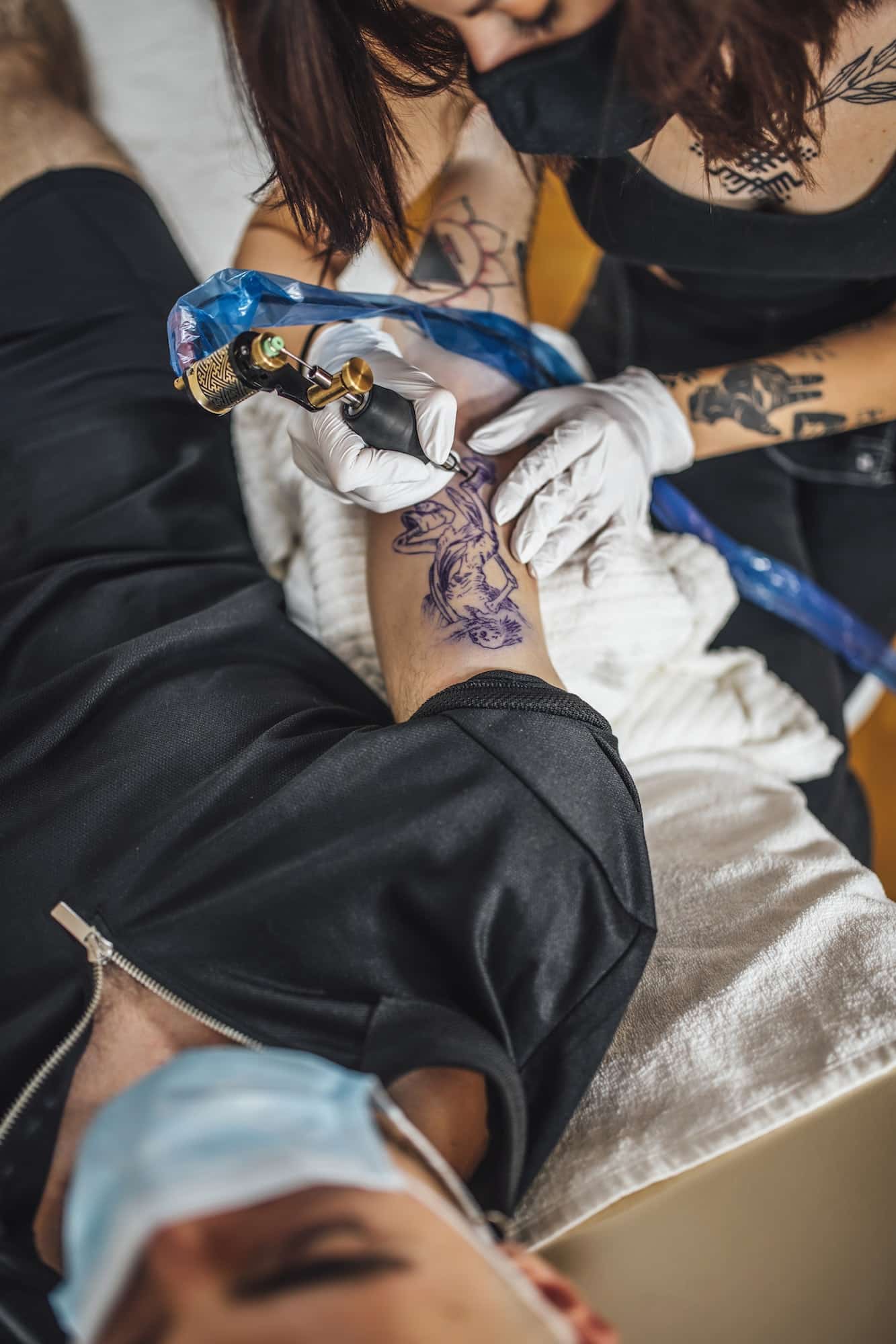 Top View of Female Tattoo Master Tattooing Man’s Arm in a Studio
