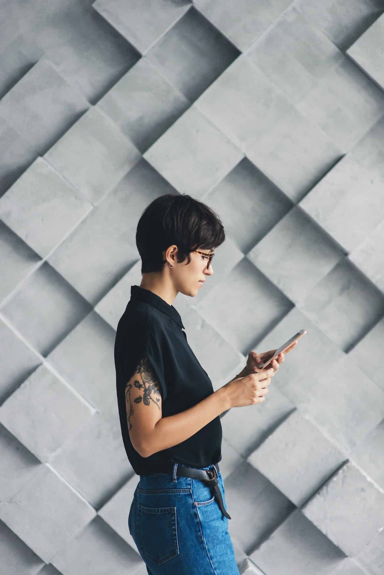 Young woman in glasses with tattoo on hand using smartphone.