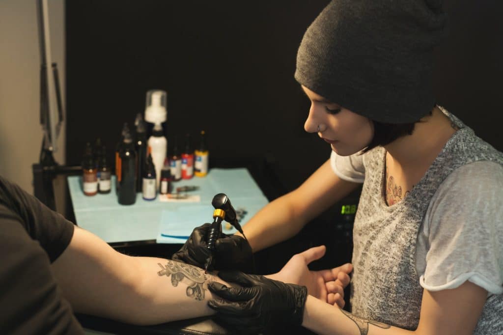 Young woman tattooist doing tattoo on male arm