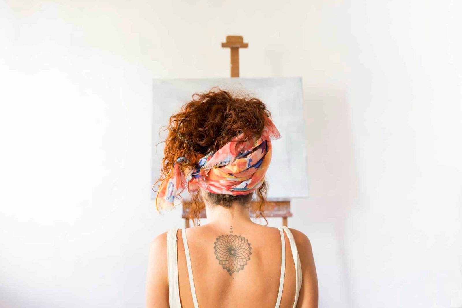 Rear view of young female painter in art studio in front of empty canvas