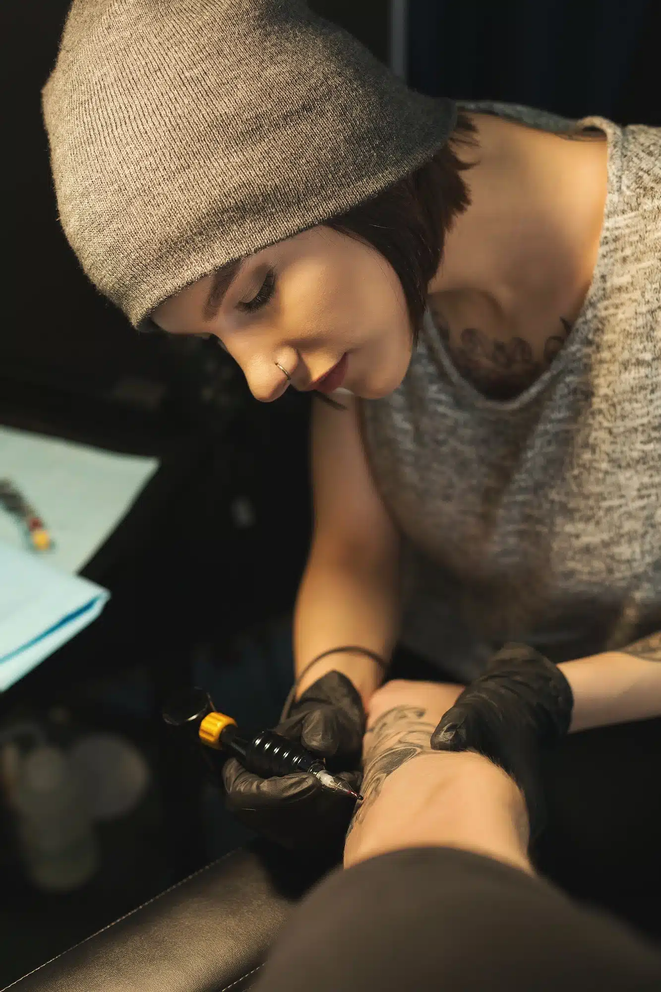 Young woman tattooist doing tattoo on male arm