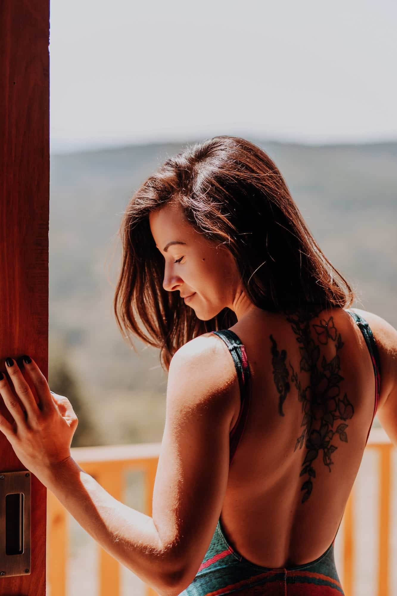 Back view of tattooed woman standing at the door of the balcony