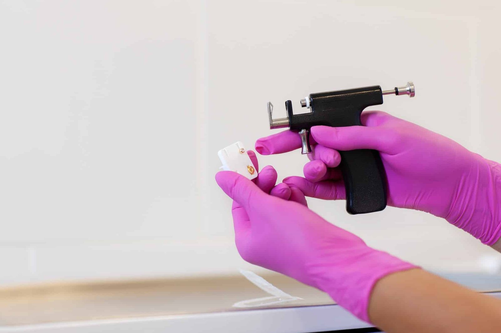 Female cosmetologist holding earrings and ear piercing gun