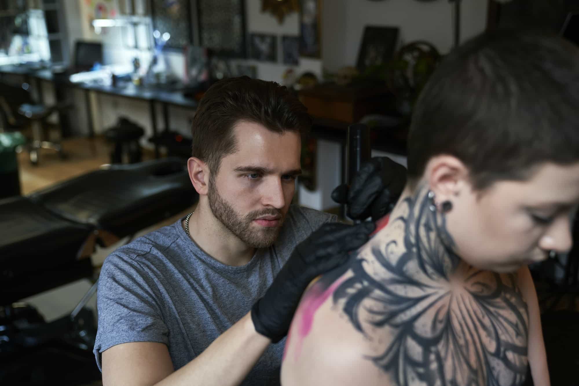 Focus caucasian man tattooing back of woman at the studio