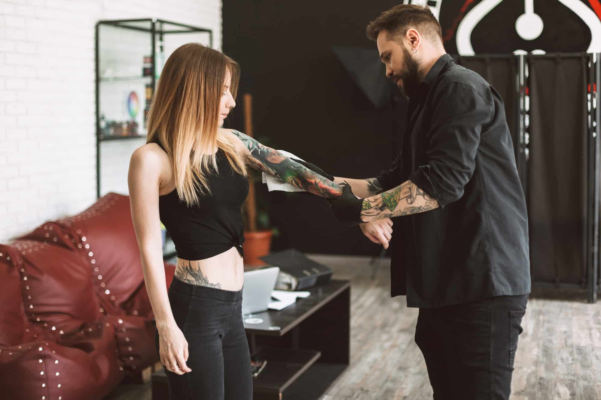 Professional tattooer and tattooed girl watching result of new t