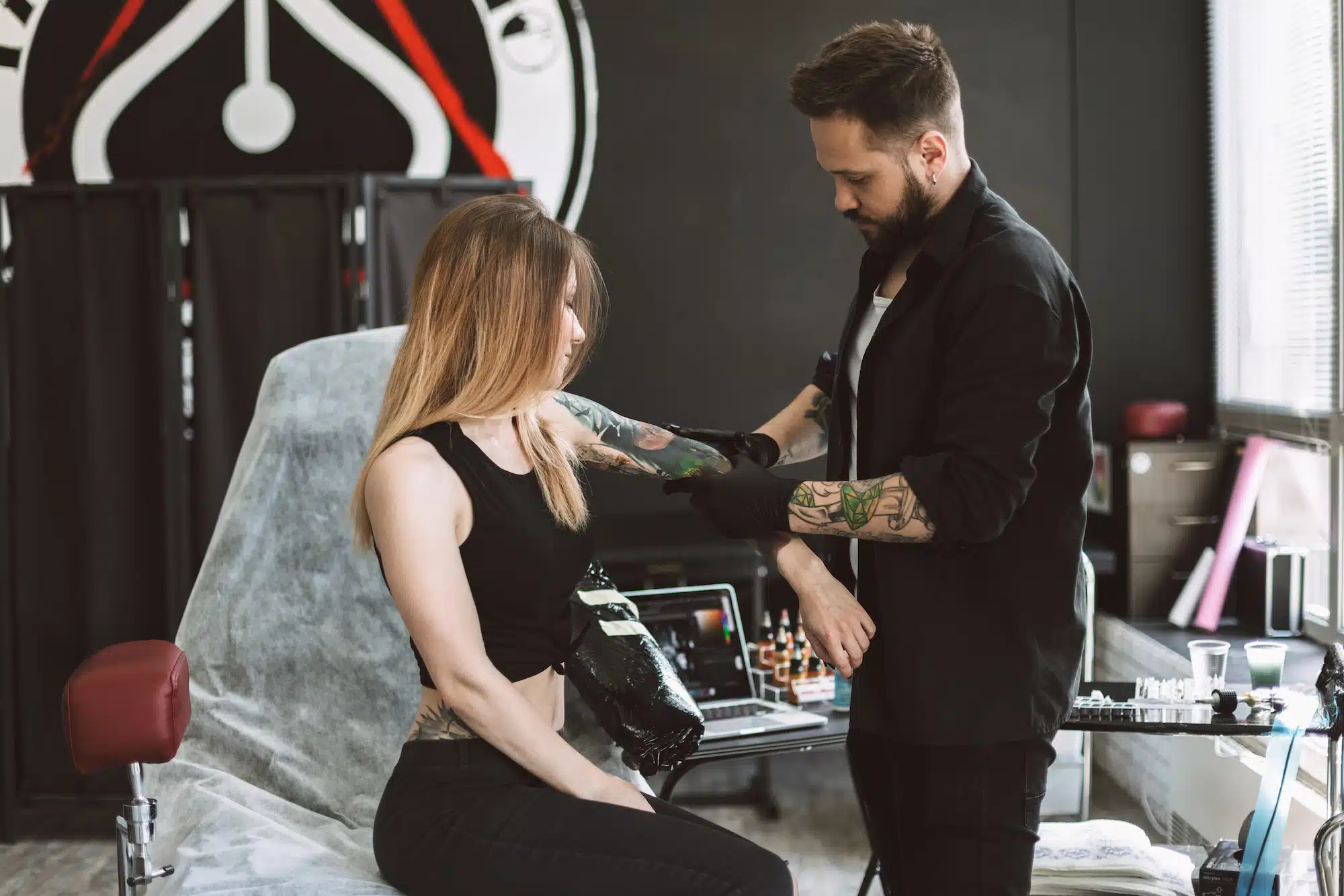 Professional tattooer discussing with girl new tattoo on hand in