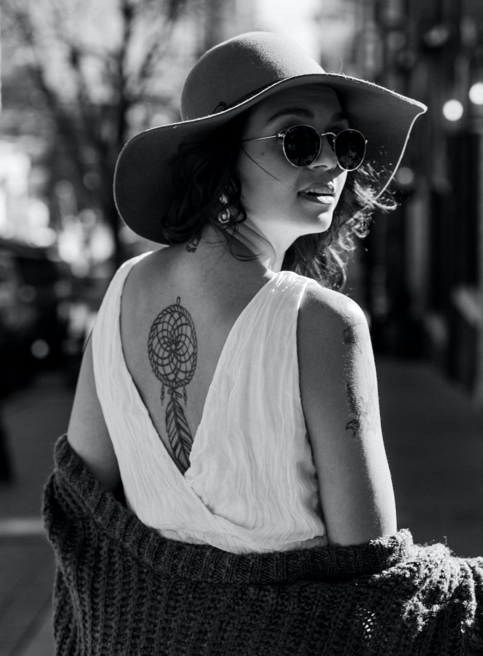 Beautiful woman in hat and white dress with the tattoo on the back