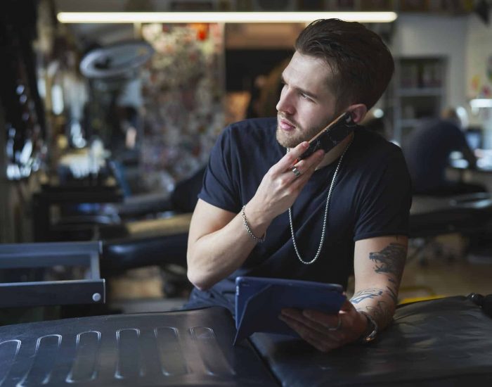 Caucasian tattoo artist talking by mobile phone and in tattoo studio