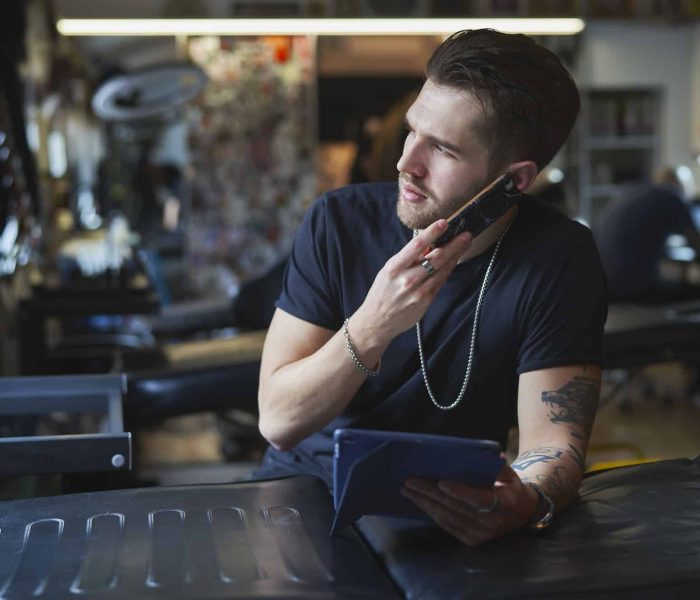 Caucasian tattoo artist talking by mobile phone and in tattoo studio