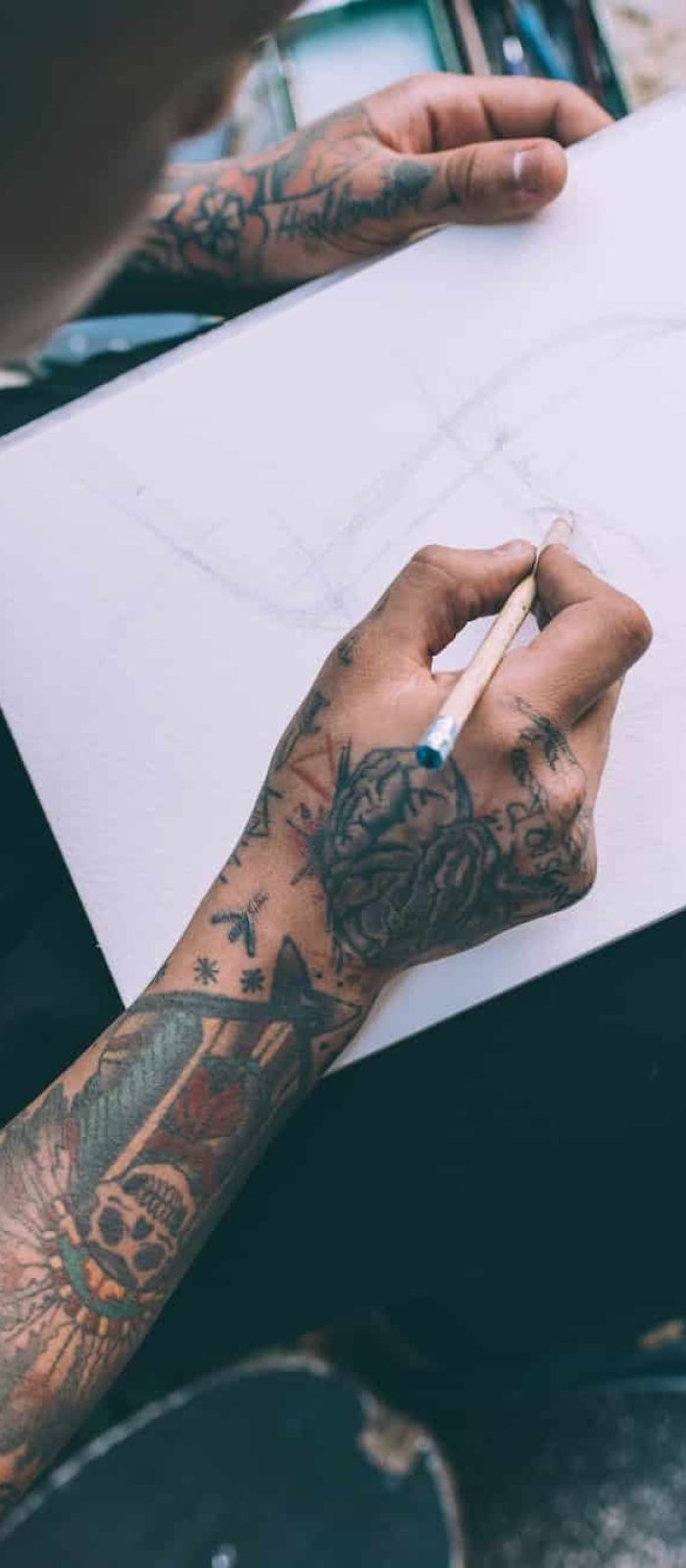 Close up on the hands of young hispanic man tattoed sketching on sketchbook