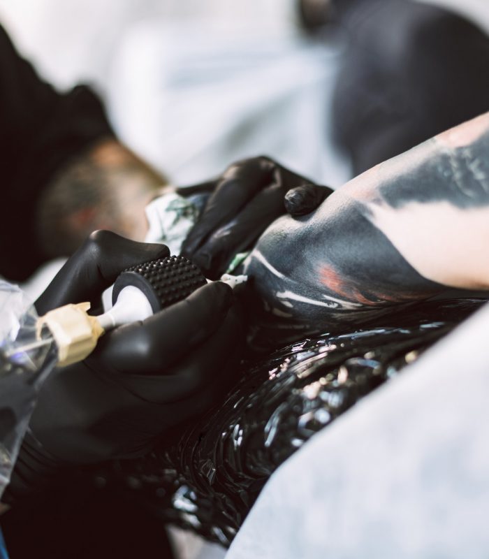 Close up professional tattooer in black gloves doing tattoo on h