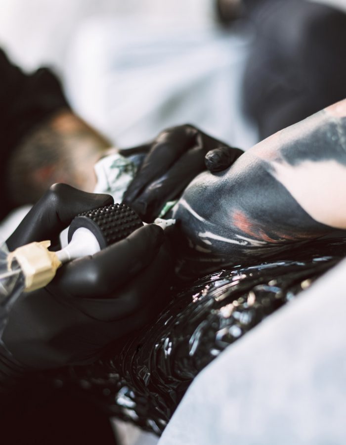 Close up professional tattooer in black gloves doing tattoo on h
