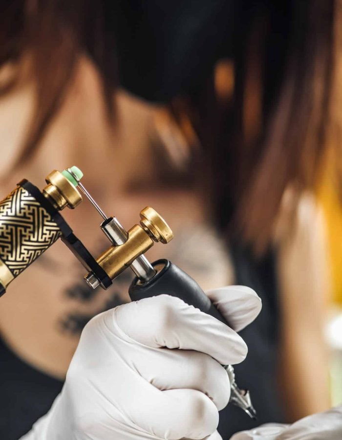 Female Tattoo Artist Prepares Tattoo Machine for Making a Tattoo on a Men’s Arm