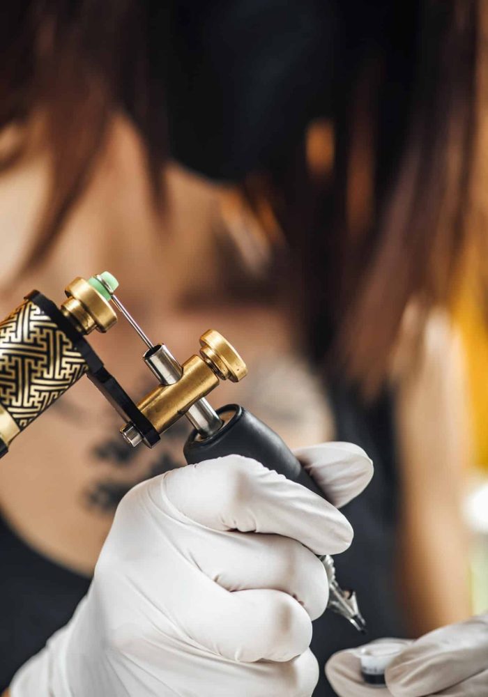 Female Tattoo Artist Prepares Tattoo Machine for Making a Tattoo on a Men’s Arm