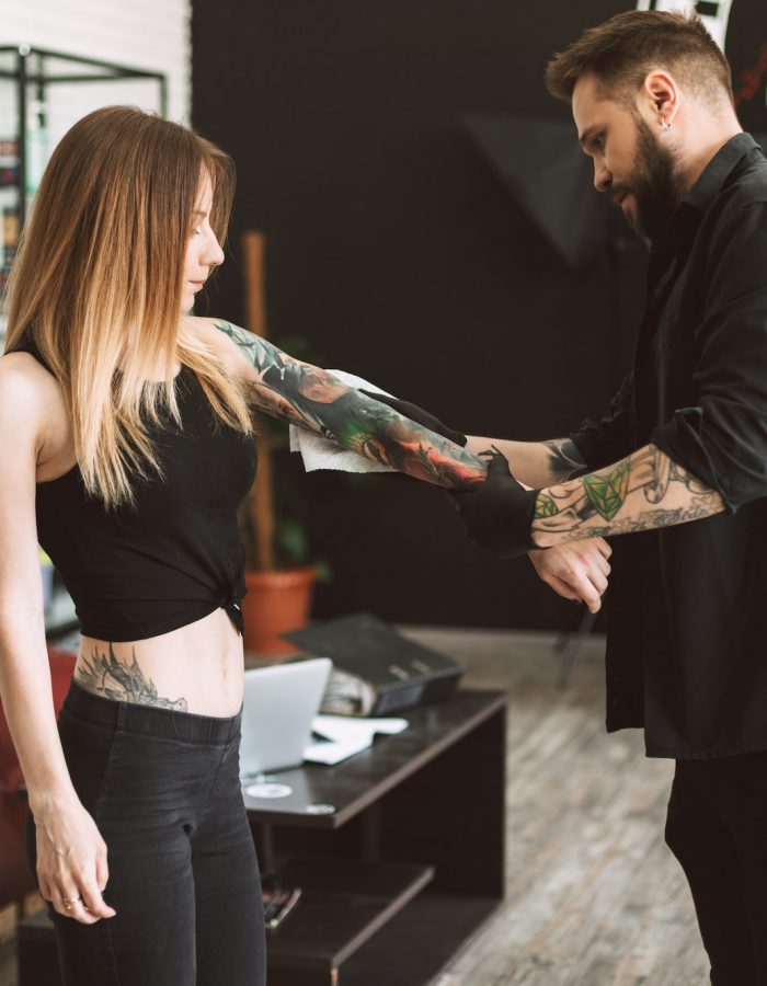 Professional tattooer and tattooed girl watching result of new t