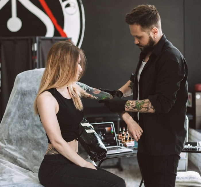 Professional tattooer discussing with girl new tattoo on hand in
