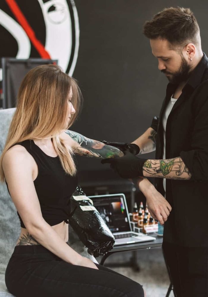 Professional tattooer discussing with girl new tattoo on hand in