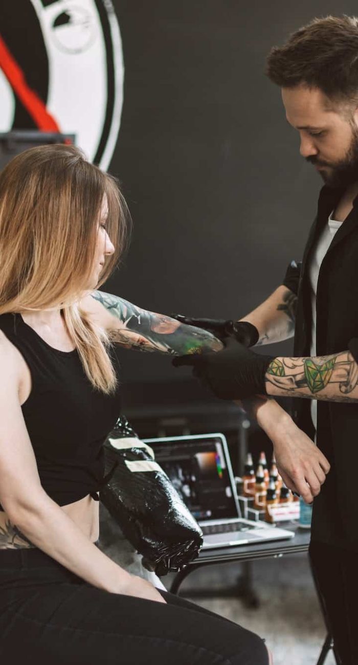 Professional tattooer discussing with girl new tattoo on hand in
