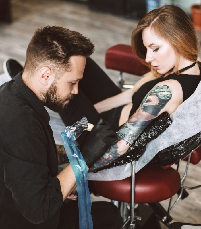Professional tattooer doing tattoo on hand by tattoo machine whi
