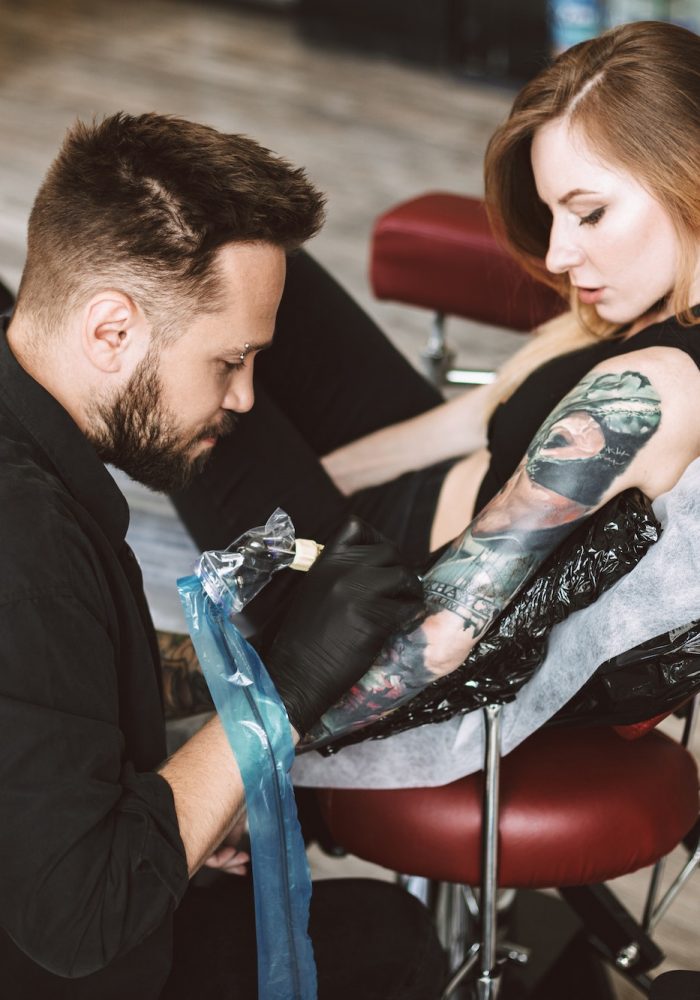 Professional tattooer doing tattoo on hand by tattoo machine whi