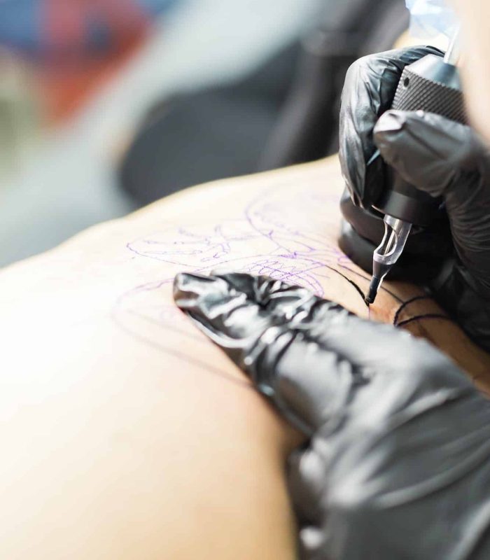 Professional tattooer make the tattoo with gloves on by special tool close up