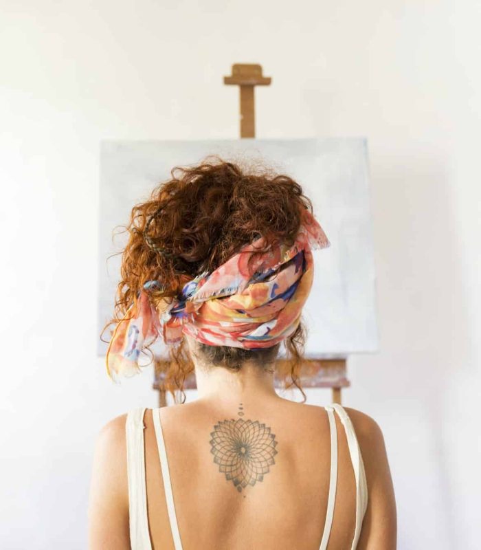 Rear view of young female painter in art studio in front of empty canvas