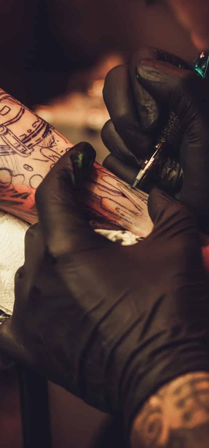 Tattoo artist working on a man's arm tattoo in a studio