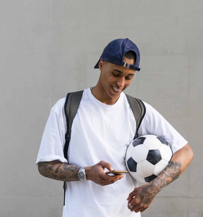 Tattooed young man with football alooking at smartphone