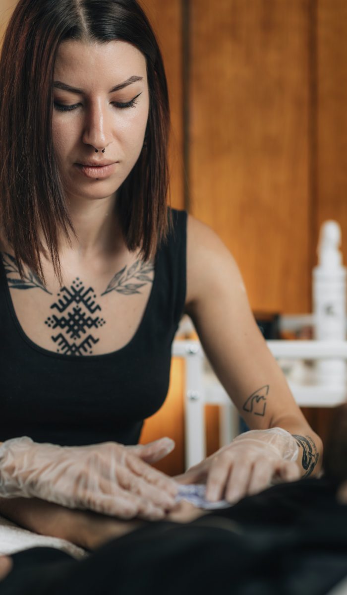 Tattooing. Female Tattoo Artist Applying Tattoo Stencil onto Male Arm before Tattooing