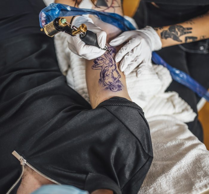 Top View of Female Tattoo Master Tattooing Man’s Arm in a Studio