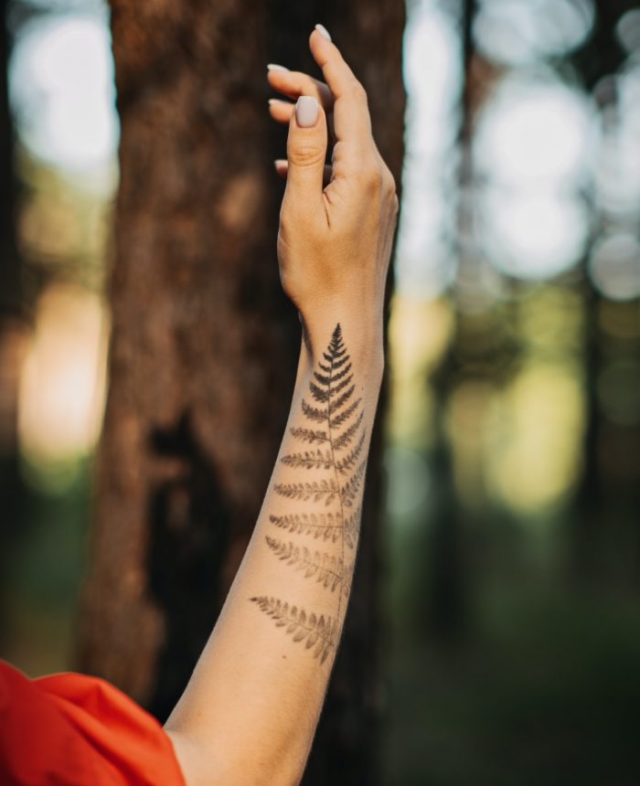 Woman with fern tattoo hugging trees and enjoying nature in the pine forest.