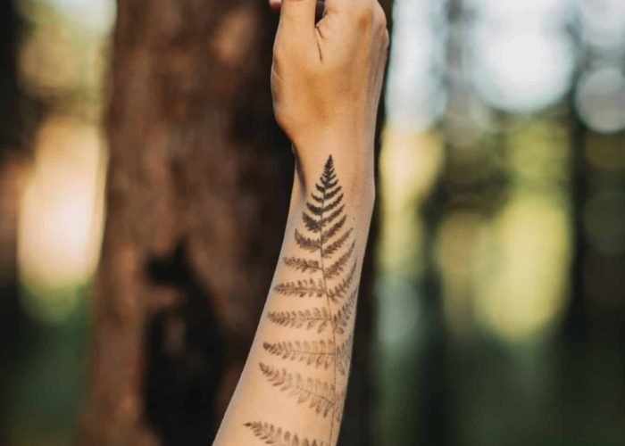 Woman with fern tattoo hugging trees and enjoying nature in the pine forest.