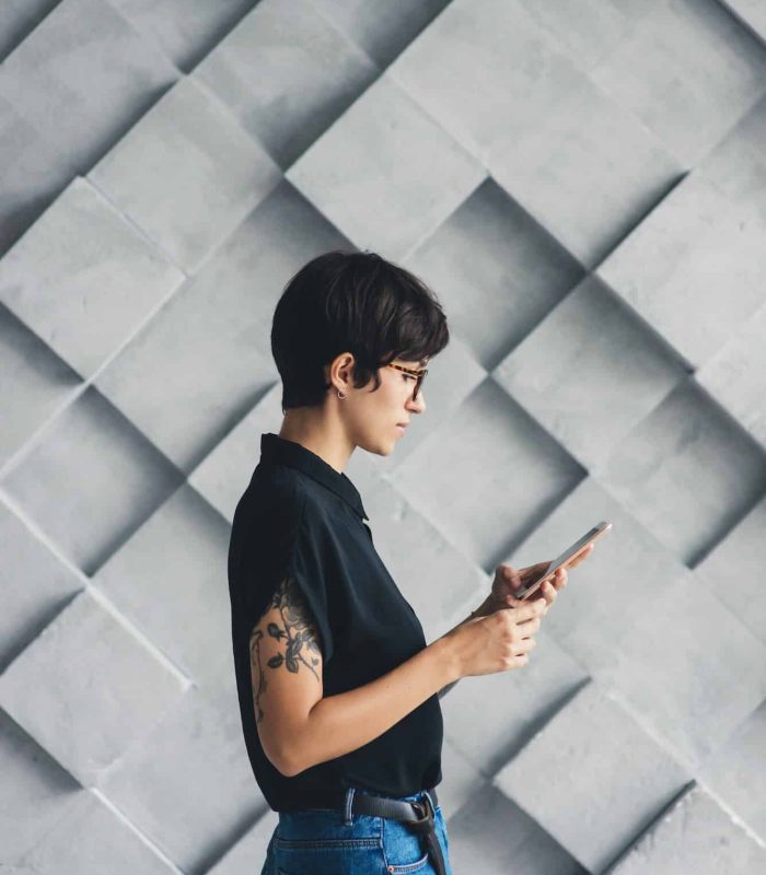 Young woman in glasses with tattoo on hand using smartphone.