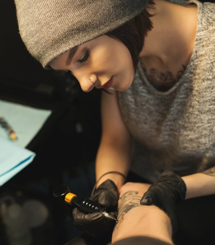 Young woman tattooist doing tattoo on male arm