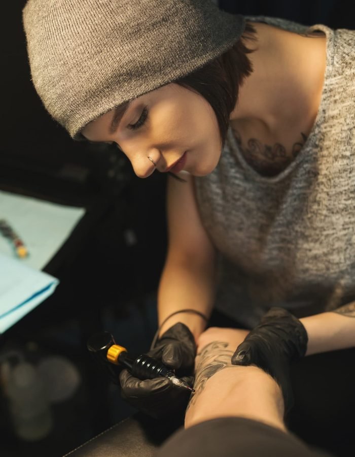 Young woman tattooist doing tattoo on male arm